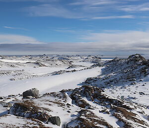 Landscape view of snow covered rocky peaks into distance with blue sky and clouds above