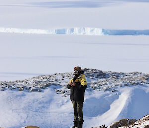 Man standing on rocky peak with ice covered bay and glacier edge in background