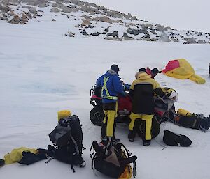 Snowy slope with injured man in bivy bag with quad bike and equipment spread across the foreground