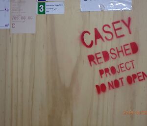 Wooden board with red stencil lettering reading “Casey Redshed Project. Do not open.”