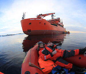Fish eye lens shot of man lying in front of inflatable boat with large orange ice-breaker behind
