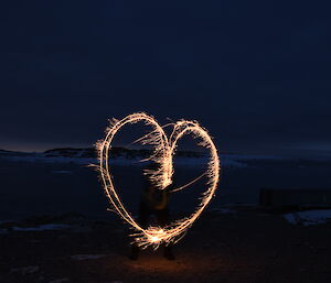 Nightime shot of landscape barely visible and heart shape light made from sparkler