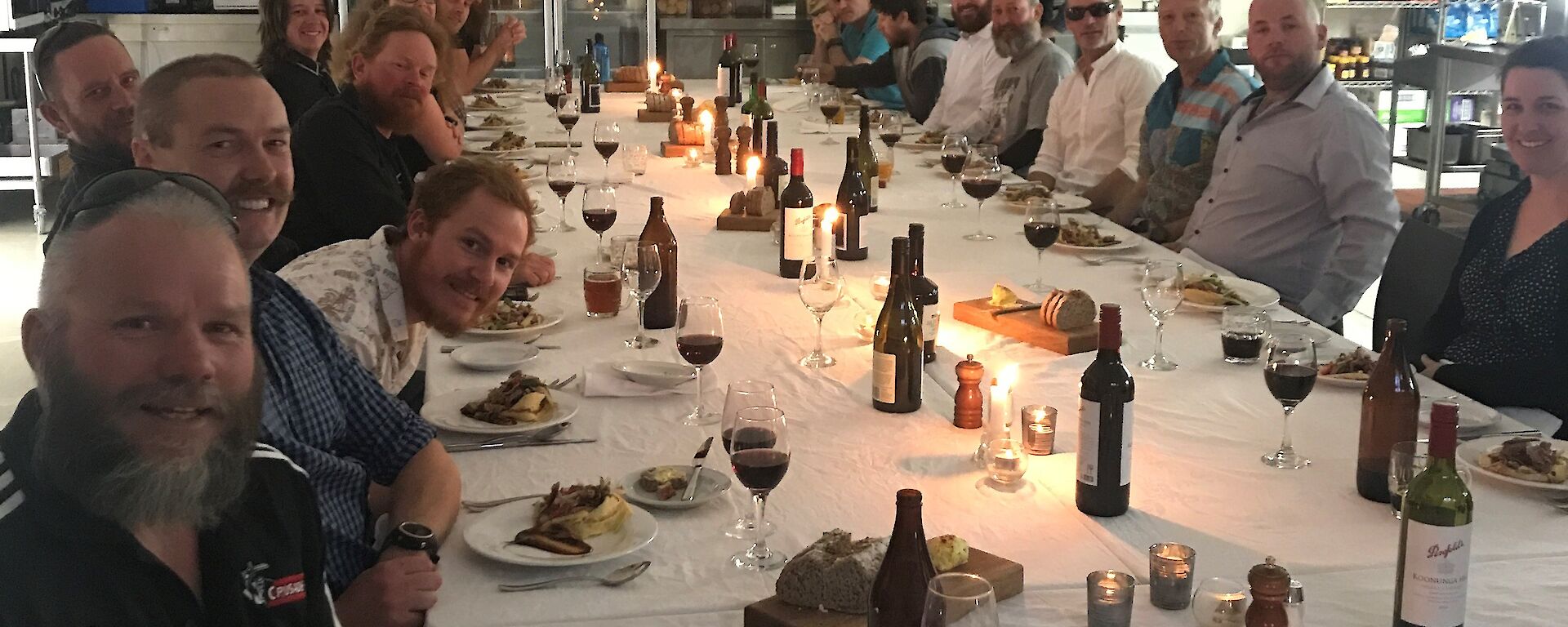 Large long table set with white tableclothes and candles, with expeditioners sitting down either side smiling towards camera.
