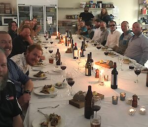 Large long table set with white tableclothes and candles, with expeditioners sitting down either side smiling towards camera.