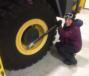 Woman in winter gear crouching near very large tyre tensioning the large wheel nuts