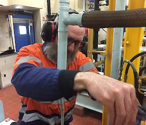Expeditioner in personal protective equipment (ear muffs and glasses) works on engine in main power house