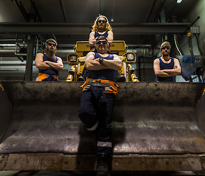 Large bulldozer in workshop with the Casey mechanics standing on the machine in blue singlets and wearing sunglasses — looking tough.