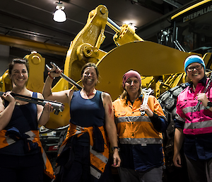 The women of Casey station dressed as mechanics holding large tools, standing in front of a bulldozer