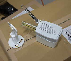 Radiosonde white plastic box with two gauges off the side attached by string to a roll of string which unwinds as balloon is released