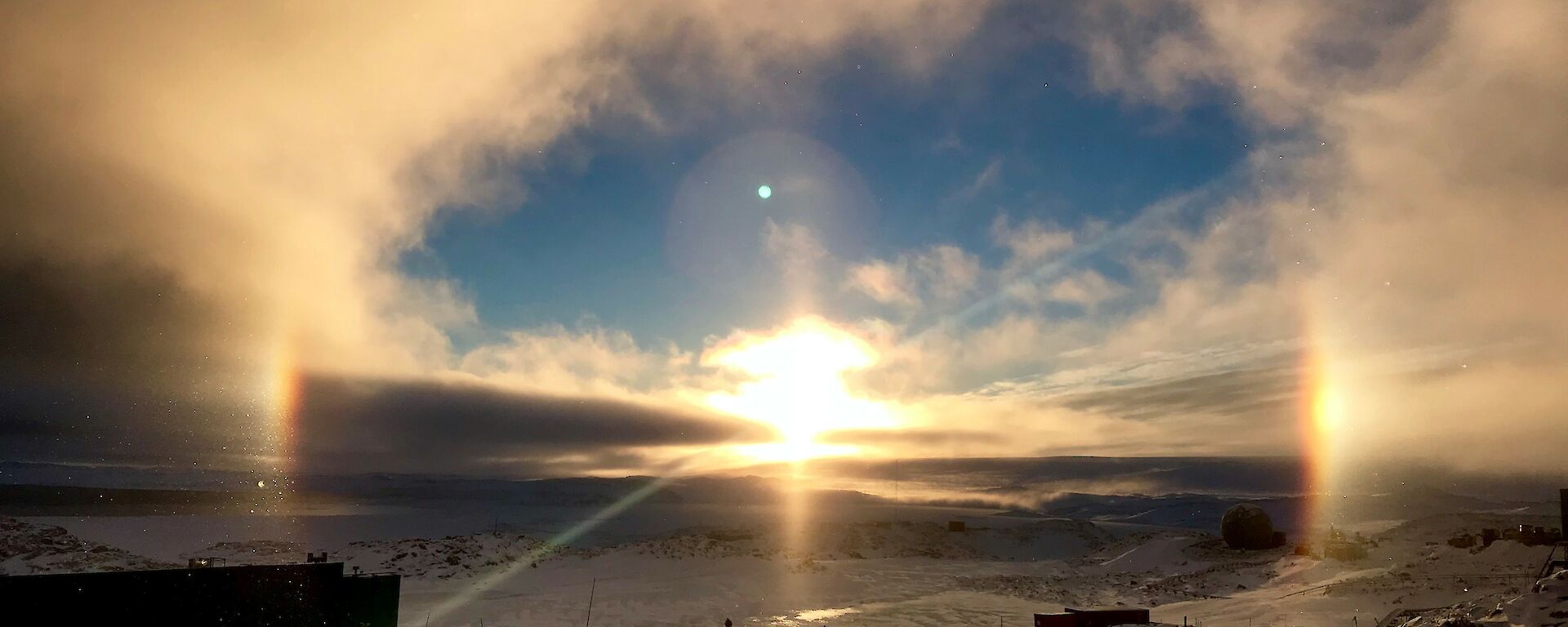 View across Newcomb Bay from Casey Station looking towards the sun coming up over the horizen with a halo created around the sun and sun dogs (mock suns) either side of the sun on the horizen