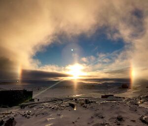 View across Newcomb Bay from Casey Station looking towards the sun coming up over the horizen with a halo created around the sun and sun dogs (mock suns) either side of the sun on the horizen