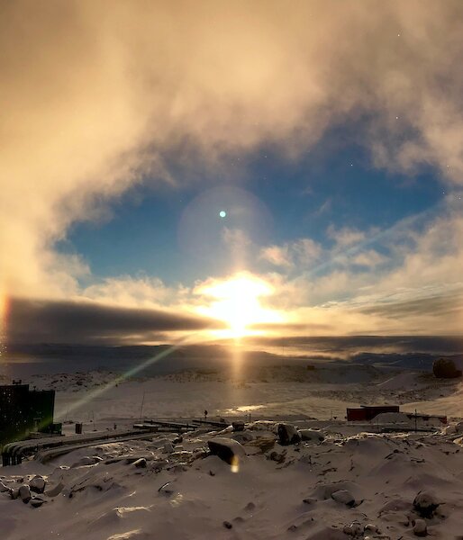 View across Newcomb Bay from Casey Station looking towards the sun coming up over the horizen with a halo created around the sun and sun dogs (mock suns) either side of the sun on the horizen