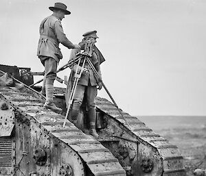 Two men with camera standing on military tank.