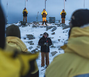 Man centre picture gives a reading, with flag party looking down and expeditioners looking on