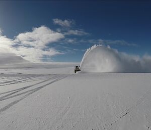 Photo taken from cab of a loader looking back along runway to second loader with large plume of snow blowing up into the air
