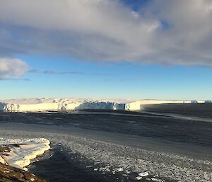 Edge of a glacier as it breaks out over a large bay, pancake sea-ice forming in the foreground, blue sky with clouds above