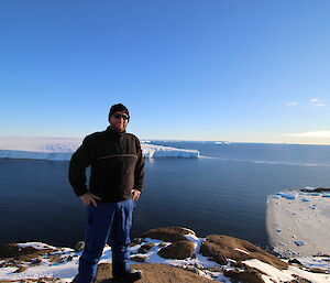 Expeditioner standing in foreground on rocky outcrop, overlooking sea and glacier tongue exending out into the sea