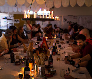 Long table laden with food and pig on spit at centre, candle laden chandeliers hanging above and people sitting around table in variety of medieval costumes