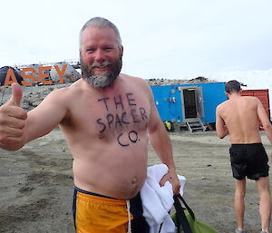 Man standing in shorts with “The Spacer Co” painted on chest, smiling and giving a thumbs up