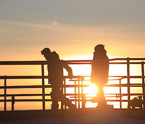 Men standing on top of the fuel tanks amongst handrails with the sun rise silhouetting them