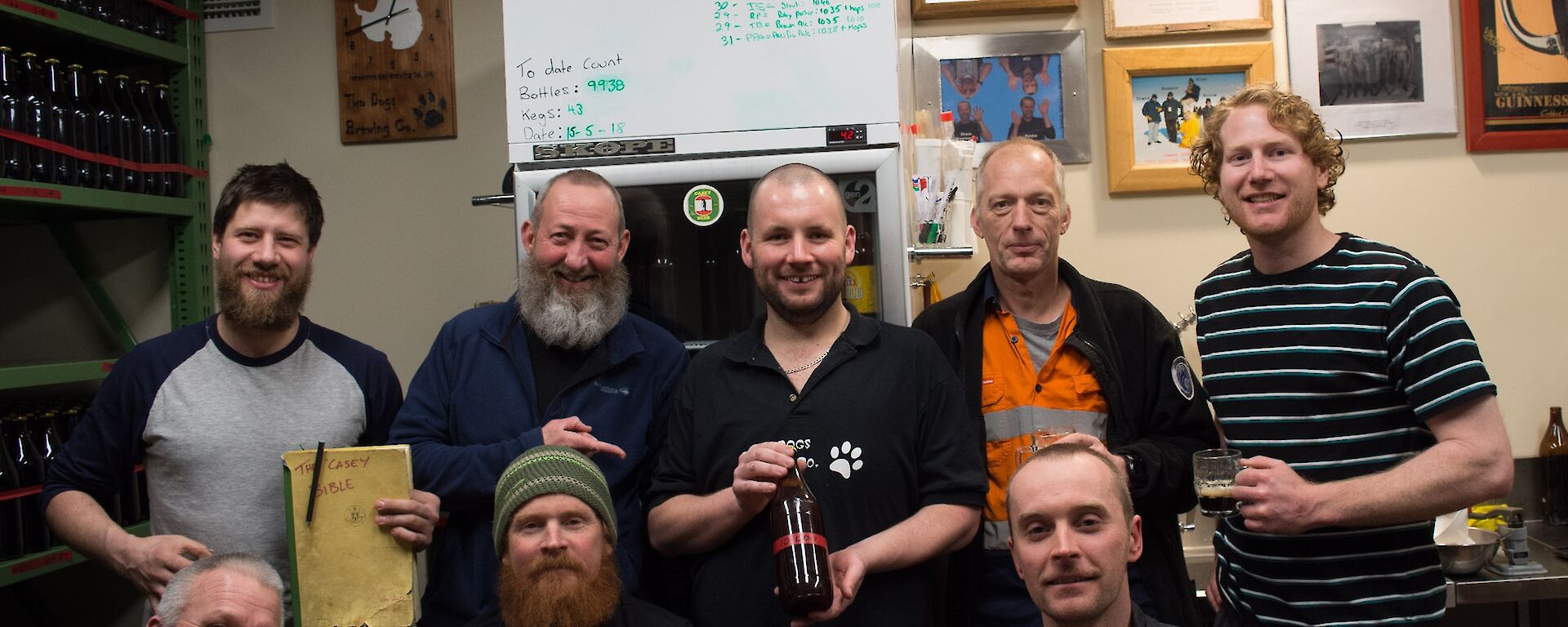 Group of men in brew room with centre man holding a brown beer bottle with red tape reading 10000 on it
