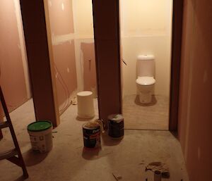 Three toilet cubicles with rough plaster board all empty except one on right has a toilet installed