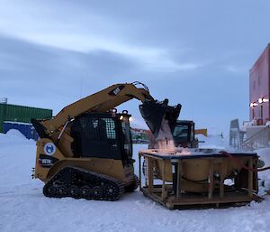 Outdoor spa positioned on snow in front of RedShed to right of picture, to the left a yellow/black skid steer is dumping snow into the spa