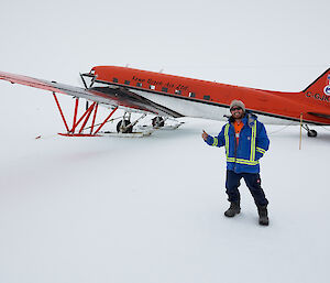 In foreground man standing smiling giving a thumbs up, in background Basler aircraft on ice runway, basler is white bottom half and red to half