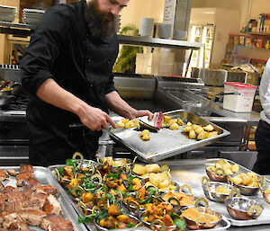 Chef behind large kitchen bench which is laden with food