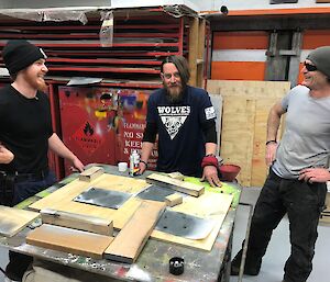 Three men standing around a workbench in the workshop, On the bench are stencils of snowflakes