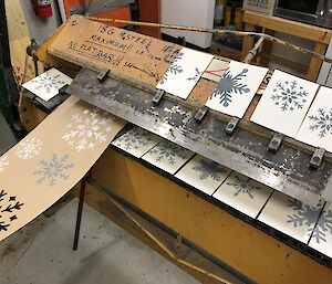 Finished product of the stenciling, snowflakes stencilled onto menu cards and tablerunner, drying out on workshop lathe