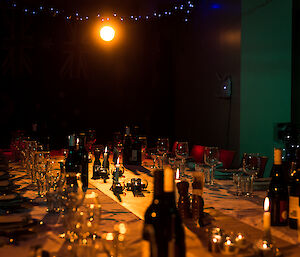 Looking down the long table all set for dinner, shiny crockery, cutlery and glasswear, down the cntre of the table are lit candles and tealights, and abover blue and white fairy lights