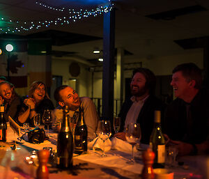 A laughing group of expeditioners sitting at the table under dim lighting