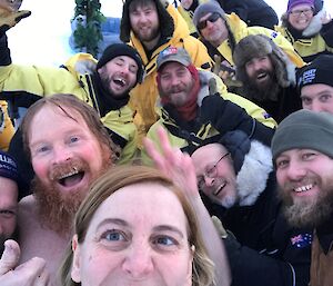 A self taken after the swim, a group of 14 expeditioners all rugged up and smiling and waving at the camera