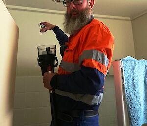 Man in high vis stands on ladder holding fire testing implement under fire sensor on ceiling