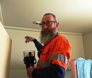 Man in high vis stands on ladder holding fire testing implement under fire sensor on ceiling