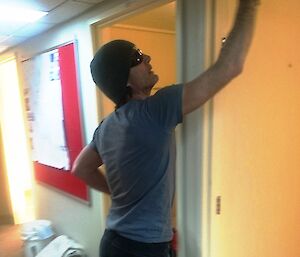 Man standing in hallway is sanding top frame of the door leading into a bedroom