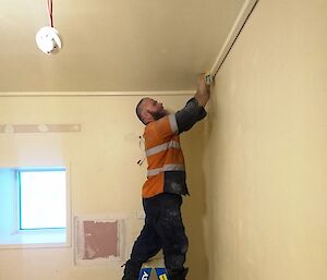 Man standing on short ladder in corner of room is sanding the walls
