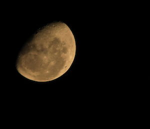 A close up of the moon, showing craters and dark patches in top left of picture, rest of picture is black