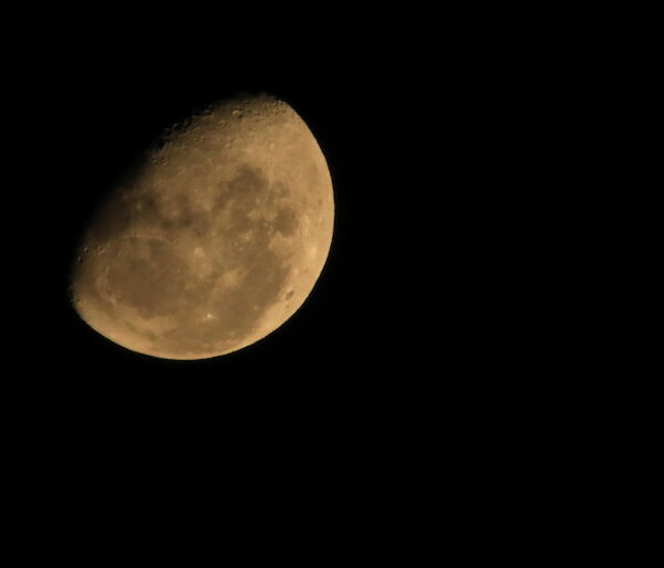 A close up of the moon, showing craters and dark patches in top left of picture, rest of picture is black
