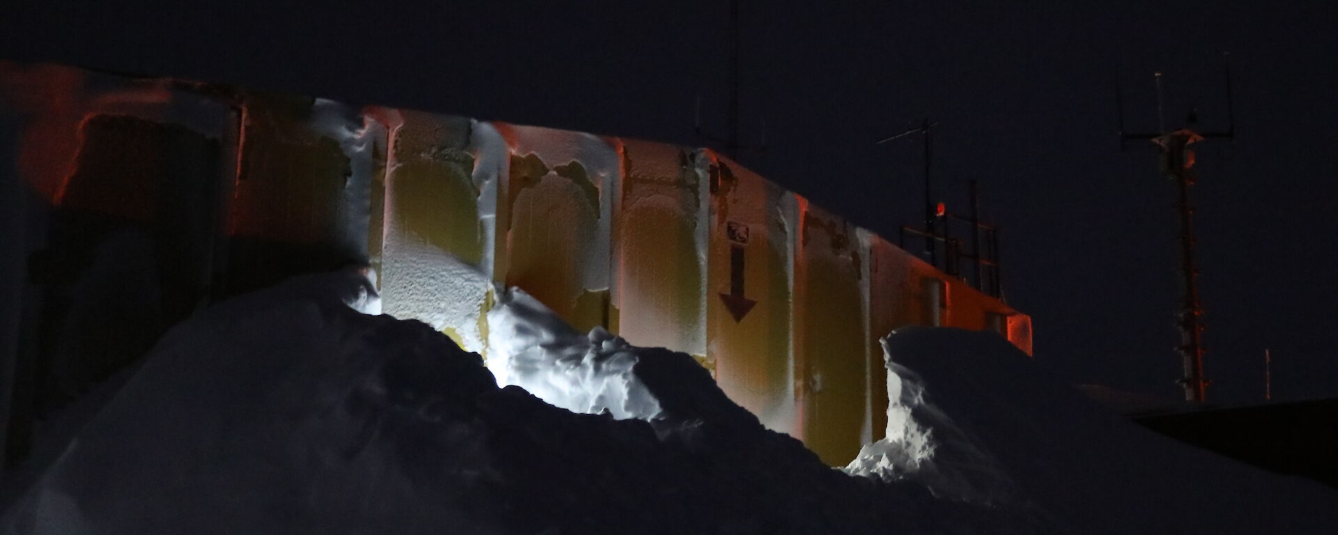 Side of a yellow building showing large bank of snow built up almost to the top of the building
