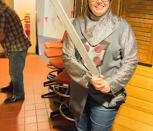 Woman dressed as a knight wearing helmet and holding large wooden sword
