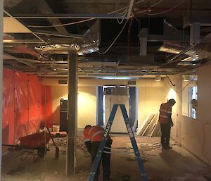 Large room as building site, rubble on floor, ceiling tiles removed, red plastic screening down left hand side