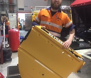 Man in workshop wearing high vis shirt holds a yellow painted panel of the loader