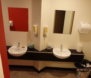 Inside bathroom looking at double sinks in vanity along length of wall, with mirrors above and soap and paper towel dispensers