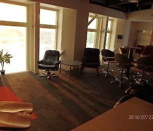 Indoor view of seating in a bar area, groups of tables and chairs, carpeted floor, windows on far wall