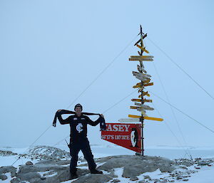 Man wearing Carlton merchandise (Jumber and Scarf) stands beside the Casey sign on rocky outcrop
