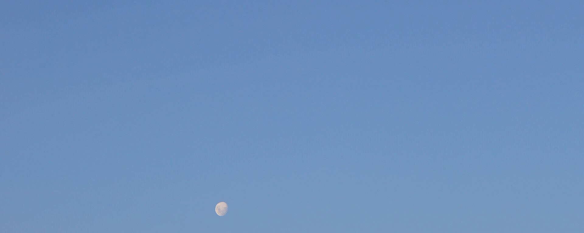 Foreground a green domed building on rocky outcrop. Above clear blue skies with full moon in white centre picture