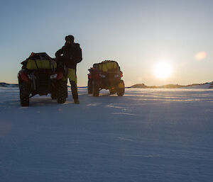 Two quad bikes and man sillouetted against the sunset on snow covered ground