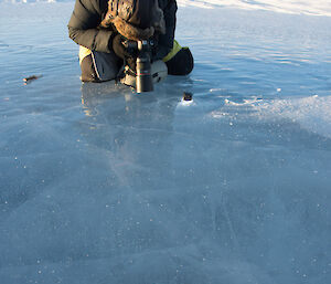 Man knelling on frozen ice taking photo down into the ice